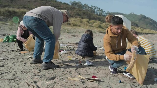 Young man picking up trash with group of volunteers on the beach