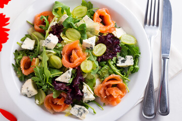 Salad of rocket, light-salted salmon, grapes and soft cheese on a plate