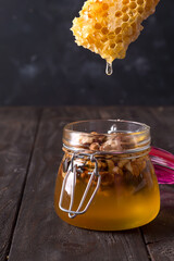 honey comb dripping from dipper into jar with nuts on old wooden table. Healthy eat