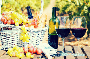 red wine ripe grapes and picnic basket on table in vineyard