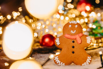 Coronavirus pandemic, conceptual background with unfocused lights christmas decorations and gingerbread in the shape of Santa Claus wearing a protective medical mask