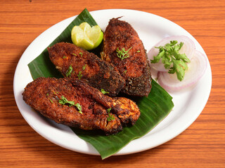 Delicious crispy King fish fry also known as indian surmai, served with onion and lemon placed over a rustic wooden background,selective focus
