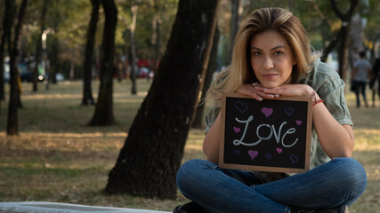 Beautiful blond girl sitting and Holding a panel with the word Love.