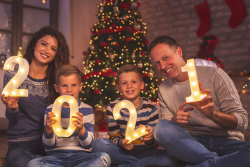 Mother, father and two boys holding illuminated numbers 2021