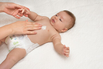 Mother applying cream or lotion on little cute cheerful baby body. Baby massage concept.