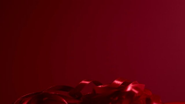 Dark red silk curly ribbon is moving and dropping on a matte ruby red backdrop. Atmospheric seamless video background. New year, Christmas, St. Valentine festive mood. 4k high quality video footage