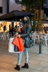 Young brunette girl with long and attractive hair, with protection mask against covid-19 shopping in shopping street with her hands full of bags
