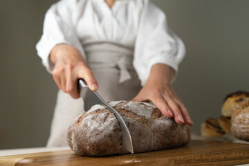  whole-grain bread put on a kitchen wooden Board with the chef holding a cutting knife. Fresh bread on the table close-up. The traditional concept of a bakery and eating healthy