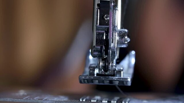 close up view of African American black hand with long nails using a sewing machine to manufacture fabric for mask creation. the thread bobber goes up and down to design pretty patterns 