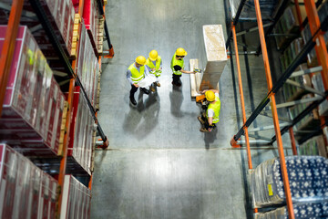 Warehouse manager and workers consult plans between tall shelves, above view