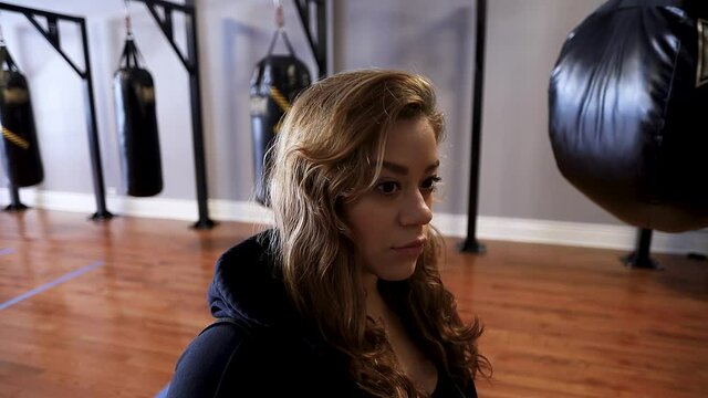 portrait  of young attractive Hispanic woman is taking off her hood in an indoor gym before beginning a stuff workout for health and fitness. she looks intently into the camera 