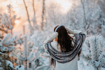 Fototapeta na wymiar A girl in a beige plaid and fur earmuffs is having fun in a fabulous snowy forest. Snowy trees. Fashionable stylish warm winter clothes. Artificial fur.