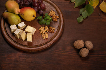 Top angle view. Brie cheese with fruits, grapes, walnuts on a dark wooden plate and wooden board. Wine snacks set: selection of cheese, grapes, pear and three walnuts on a wooden table. 
