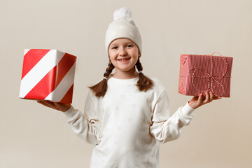 Happy little girl in a hat and sweater shows gifts on a white background.