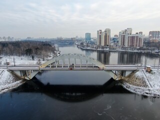 Aerial view panorama of the railway bridge across the river against the background of the city in winter. Travel by rail.