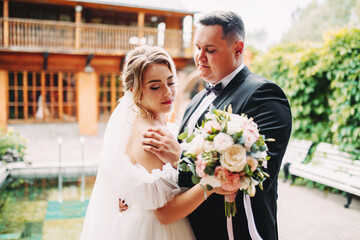 Wedding couple hugs, elegant groom and tender bride with luxurious bouquet of roses