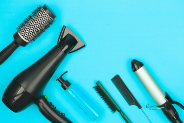Hairdressing tools in black: hairdryer, combs, sprays, curling iron on a blue background, space for text, flat lay
