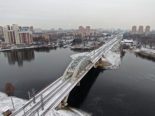 Aerial view panorama of the railway bridge across the river against the background of the city in winter. Travel by rail.