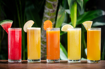 mixed fresh organic fruit juices glasses on sunny garden table - 397006095
