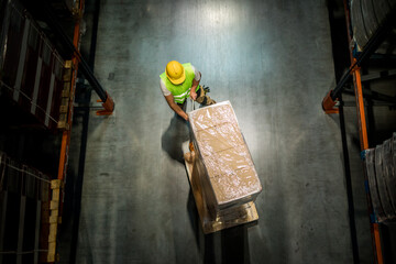Warehouse worker pulling a pallet truck between shelves, above view