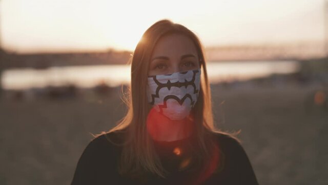 Face of young woman on the beach during the amazing sunset who is wearing a cloth mask and is turing left.