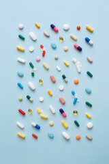 Creative layout of colorful pills and capsules on blue background. Minimal medical concept. Pharmaceutical, Covid-19 or Coronavirus. Flat lay, top view