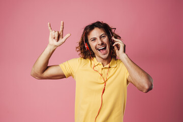 Obraz na płótnie Canvas Excited guy listening music with headphones and showing horns gesture