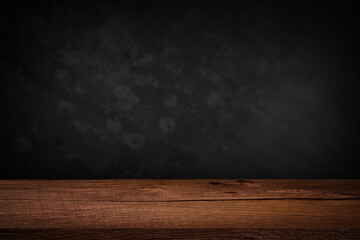 Free space on a wooden table for displaying products with a blurred black wall background.