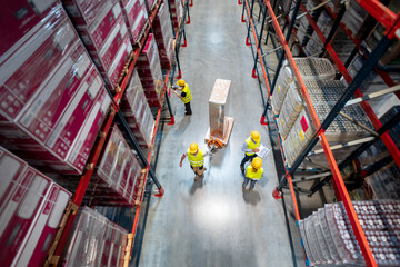 Warehouse workers at work between rows of tall shelves full of packed boxes, top view