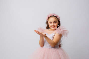 little girl in a beautiful fancy dress blowing on confetti on a white background