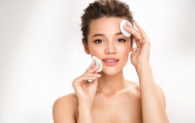 Woman removing makeup, holds cotton pads near face. Photo of woman with perfect skin on white...