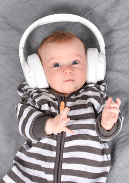 three-four months old cute caucasian baby lying on bed listening to music in big headphones and dancing. Look at camera. Music relax concept. Vertical photo.