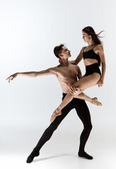 Fototapeta premium Young and graceful ballet dancers in minimal black style isolated on white studio background. Art, action, flexibility, inspiration, lightness of the body concept. Flexible caucasian ballet dancers.