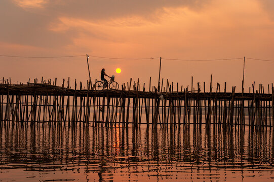 Cambodian lady on bike at sunset, Ko Paen Bamboo bridge, Kompong Cham, Cambodia. A temporary bamboo bridge is reconstructed every year to span a contributory to the Mekong from main city to an island.