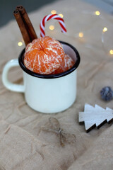 Enamel mug filled with tangerines, candy cane and cinnamon sticks and Christmas decorations. Selective focus.