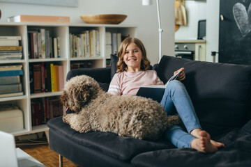 teenager girl relaxed on sofa reading book with her dog