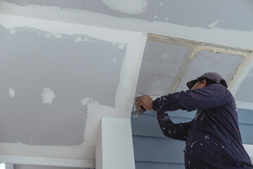 A man applies putty to the corner of the ceiling. Wearing clothes full of paint splotches. Shot at...