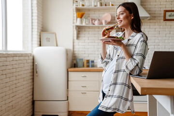 Pregnant happy woman smiling while eating sandwich
