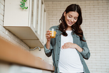 Happy charming pregnant woman smiling and drinking juice - Powered by Adobe