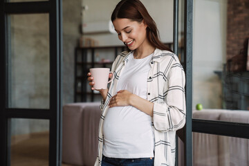 Beautiful happy pregnant woman smiling and drinking coffee
