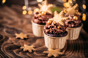 Chocolate cupcakes with star shaped cookies on a wooden background. Christmas mood. Sweets for any occasion. In the background are yellow lights from the garland