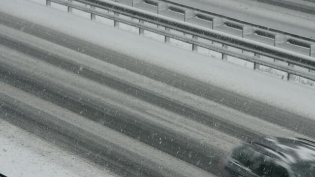 Wide locked down shot of trucks , vans and cars driving on a highway in snowfall.