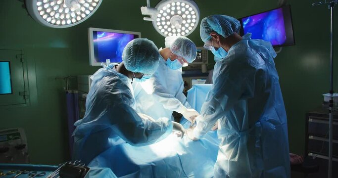 Mixed-races team of professional doctors surgeons in uniform performing neurosurgery operation under bright lamps passing medical instruments in operating room in hospital. Healthcare concept