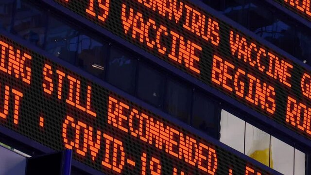 Close-up view of a fictional Times Square stock market news ticker reporting that a COVID-19 Coronavirus vaccine was approved and rollout has begun.	