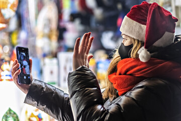 A woman with long hair in a Santa hat communicates on a smartphone via video communication. Congratulates relatives on Christmas and shows a gift. New Year's streets
