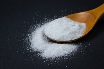 Wooden spoon with salt. Some salt is spilled nearby. Excessive salt intake. Coarse salt