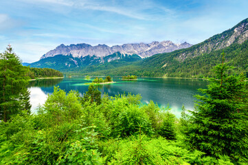 Obraz na płótnie Canvas Small islands with pine-trees in the middle of Eibsee lake with Zugspitze mountain. Beautiful landscape scenery with paradise beach and clear blue water in German Alps, Bavaria, Germany, Europe.