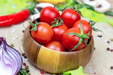 Fresh red ripe cherry tomatoes in wooden bowl with salad leaves, onion, pepper, champignon mushrooms, spices and salt on light food background.
