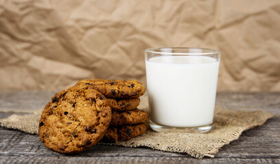 Glass with milk and oatmeal cookies on burlap on a wooden background.