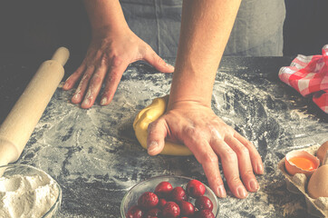 The man's hands knead the dough for the preparation of cherry strudel